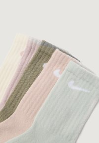 Cinci perechi de sosete cu nervuri, de lungime medie, în nuanțe de crem, roz deschis, verde măslin, roz prăfuit și verde mentă, fiecare având un mic logo alb în formă de swoosh aproape de vârf.
