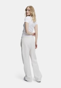 Valkoinen istuva t-paita ja vaaleanharmaat, löysät collegehousut, joissa on joustava vyötärö. Kangas on sileä ja pehmeä.