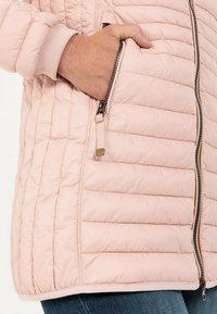 Veste matelassée rose clair avec une poche zippée, des poignets côtelés et une texture lisse. Idéale pour le superposition par temps frais.