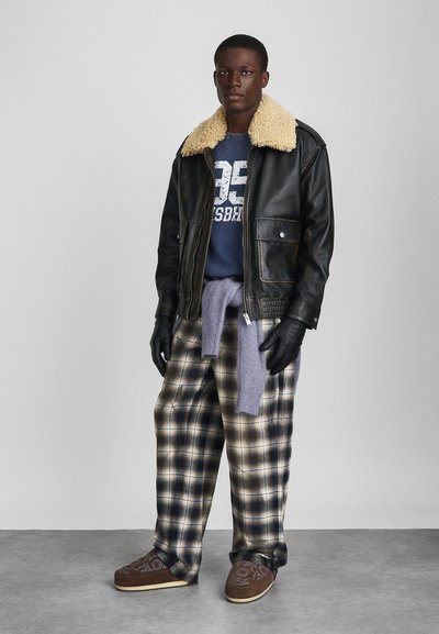 Veste en cuir noire avec col en peau de mouton, sweat gris, pantalon à carreaux, pull violet noué à la taille, gants noirs et chaussures brunes avec motif.