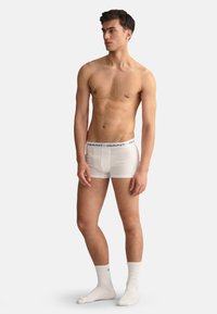 Boxeri scurți din bumbac alb cu un tiv elastic albastru pe care este înscris numele brandului, purtați de un model într-o poziție neutră.