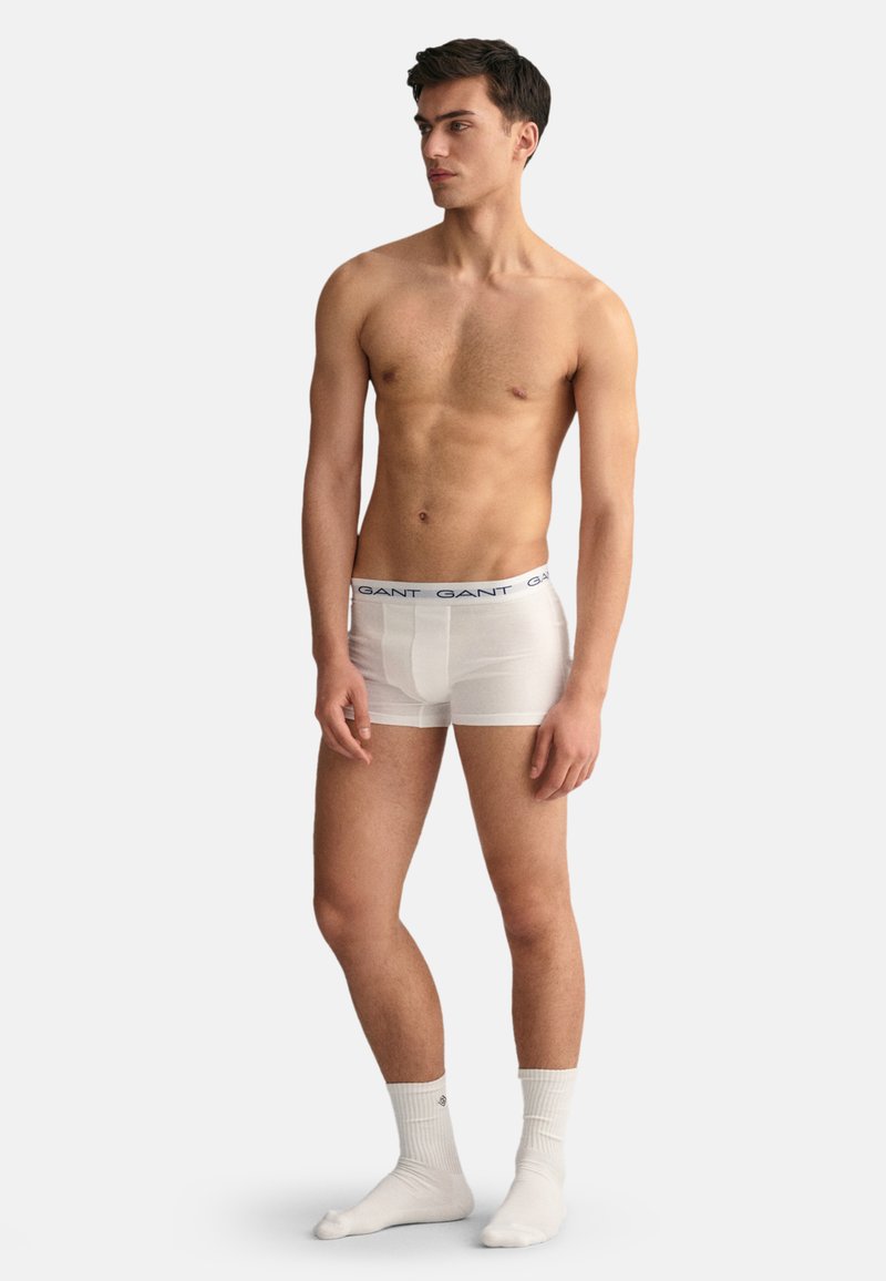 Boxeri scurți din bumbac alb cu un tiv elastic albastru pe care este înscris numele brandului, purtați de un model într-o poziție neutră.