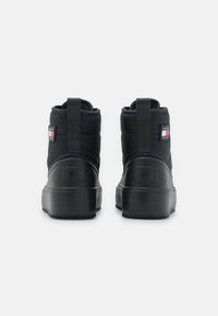 Botas negras de tobillo con un diseño acolchado, suela de goma, parche con logo y tirador en la parte trasera para ponérselas con facilidad. La textura parece suave y duradera.