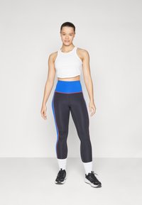 Czarne legginsy z niebieskimi i czerwonymi paskami po bokach, w zestawieniu z białym krótki topem. Stylizowane z czarnymi butami sportowymi i białymi skarpetkami.