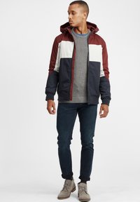 Fargeblokkerte jakke med burgunder, marineblå og kremfargede paneler. Grå strikkegenser under. Slim-fit jeans og lysegrå støvler.