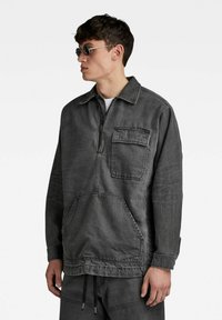 Sivkasta jeans pulover s prednjim zadrgo, z zaklopnim žepom in velikim sprednjim kenguru žepom. Ima ovratnik in dolge rokave.