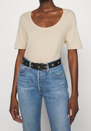 Beżowy t-shirt z krótkim rękawem i szerokim dekoltem, zestawiony z wysokim stanem jasnoniebieskich dżinsów oraz czarnym paskiem ze srebrną klamrą.