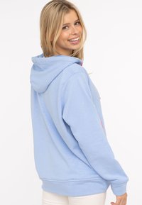 Haut à capuche bleu clair avec un cordon de serrage, présentant une poche kangourou et des accents colorés. Tissu doux, coupe décontractée et manches longues.
