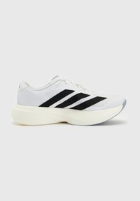 Chaussure de sport blanche avec des rayures diagonales noires et une semelle épaisse crème sur un fond uni gris clair.