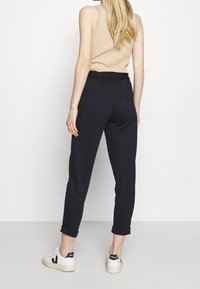 Svarta, smalnande mjukisbyxor med dragsko i midjan, muddar vid anklarna och mjukt material, tillsammans med vita sneakers med svarta detaljer.