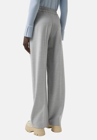 Pantalon gris à jambes larges avec une finition texturée et une taille élastique, accompagné de chaussures beiges à semelle épaisse. Détails visibles au dos.