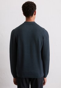 Dunkelblauer Pullover mit strukturiertem Strickmuster, langen Ärmeln und geripptem Halsausschnitt, von hinten betrachtet.