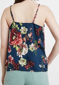 Blommig topp med marinblå bakgrund, som har stora röda och vita blommor, tunna axelband och en avslappnad passform. Slät sating textur.