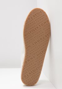 Semelle d'une chaussure beige embossée d'un motif de texte répété "TOMMY HILFIGER" sur un fond clair.