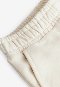 Pantaloni in cotone color crema con vita elastica arricciata e tasca laterale, con una finitura in tessuto morbido e testurizzato.