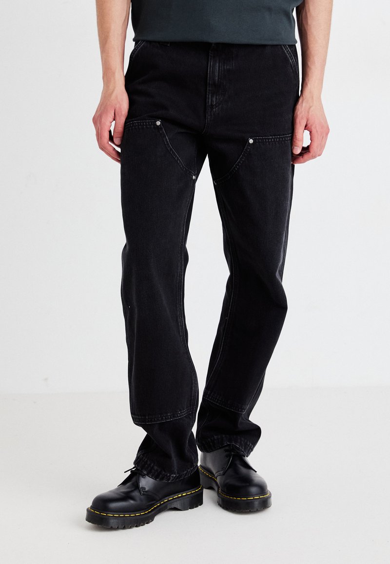 Black denim pants with a relaxed fit, featuring pocket detailing, visible stitching, and a slight sheen. Paired with black lace-up boots.
