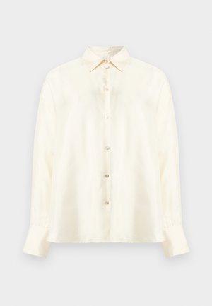 Krémová košeľa s dlhým rukávom na gombíky, so špicatým golierom a zapínacími manžetami, zobrazená na jednoduchom svetlosivom pozadí.