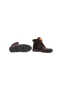 Botas de cuero marrón hasta el tobillo con una suela robusta, punta redonda, cordones en la parte frontal y una correa decorativa con una hebilla. Detalles de superficie texturizada.