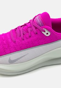 Ljubičasta sportska cipela s prozračnim pletenim gornjim dijelom, teksturiranim vezicama i bijelim međupotplatom s sivim Nike logoom.