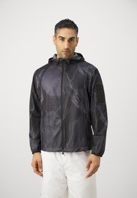 Svart jacka med tryck som har ett geometriskt mönster, huva, dragkedja och elastiska ärmslut. Tillverkad av lätta, texturerade material.