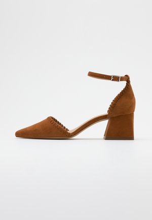 Bruine suède schoen met een puntige neus, enkelriem en blokhak. Heeft decoratieve stiksels langs de zijkanten.