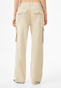 Beige cargo-housut, joissa on rento malli, kaksi takataskua, sivutaskut ja sileä, pehmeä rakenne.