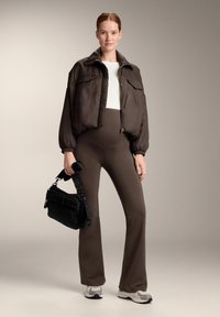 Rjava, prevelika bomber jakna z napihnjenimi rokavi čez belo majico. Rjave razširjene legice in sive superge. Črna torbica čez ramo z dodatki.