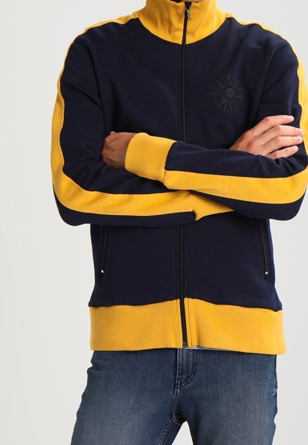 Marinblå zip-jacka med gula randiga detaljer. Har en hög krage och en centralt tryckdesign. Tillverkad av mjukt, texturerat tyg.