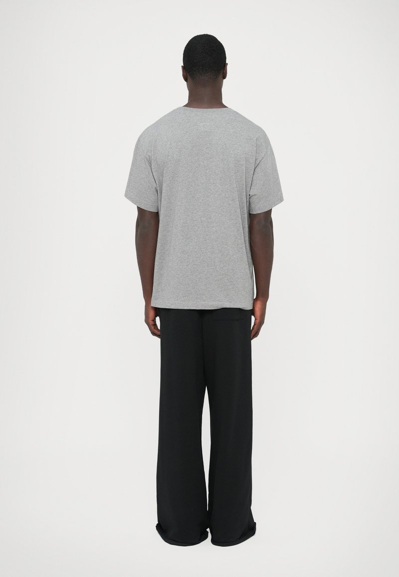 Gray cotton t-shirt with short sleeves, relaxed fit, and round neckline, paired with loose-fitting black trousers, shown from the back.