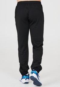 Sorte træningsbukser med elastisk talje, tapered ben og sidelommer, parret med blå og hvide sneakers med strukturerede såler.