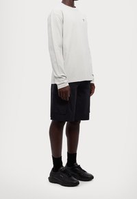 Hellgraues Langarmshirt, schwarze Cargo-Shorts und schwarze Sneakers mit goldenen Akzenten. Einfaches Design, glatte Textur und lässige Passform.