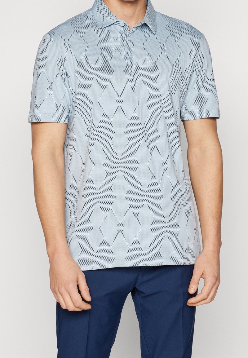 Polo bleu clair avec un motif en relief en forme de losanges de couleur bleu foncé. Manches courtes et col classique.