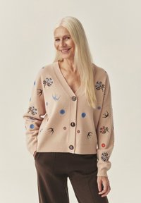 Hele roosa pehme kangaga kardigan, millel on värvikas lille- ja linnu tikand, kaheksa nuppu ees ning soonilised varrukasääred.