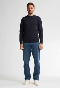 Pulover ușor de culoare bleumarin închis, cu decolteu rotund, asortat cu blugi clasici albaștri și adidași albi.