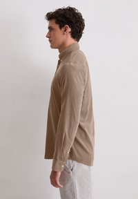 Koszula z długim rękawem w jasnobrązowym kolorze, wykonana z miękkiej tkaniny, z klasycznym kołnierzykiem i dopasowanym krojem oraz mankietami zapinanymi na guziki.