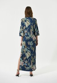 Lungo abito blu navy con motivo floreale, maniche a 3/4, spacco laterale e tessuto morbido. Caratterizzato da fiori nei colori pastello e foglie verdi.