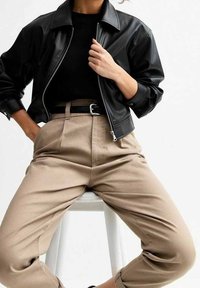 Svart kort skinnjacka med dragkedja. Fitted svart topp, högmidjade beige byxor med bälte. Släta texturer, avslappnad passform.