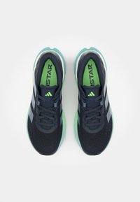 Navy blue athletic shoes with green accents, textured mesh upper, three gray stripes, and a cushioned sole. Laces are flat and dark.