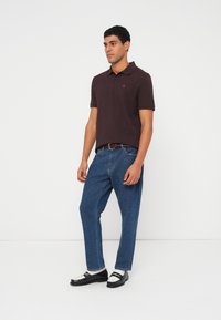 Tmavě mahagonová polokošile s límečkem, modré džínové kalhoty a černobílé boty. Jednoduchý, čistý design s viditelnými detaily švů.