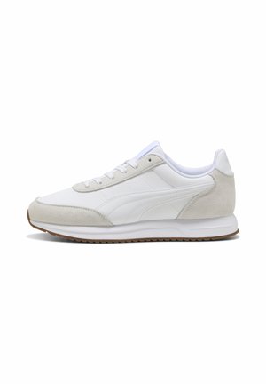 Witte lage sneaker met beige suède accenten, witte veters en een bruine rubberen zool, zijaanzicht.