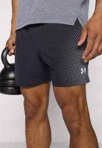 Zwarte sportshorts met een gestippeld patroon aan één kant, gemaakt van rekbare stof. Gecombineerd met een grijze tafelshirt en een zwarte kettlebell.
