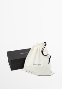 Scatola per scarpe rettangolare nera Massimo Dutti accanto a una sacca bianca con coulisse con logo Massimo Dutti e cordoncino nero su sfondo semplice.