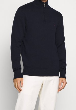 Pull marin avec zip au cou, caractérisé par un col, des poignets et un ourlet côtelés, fabriqué en tissu doux avec un discret détail de logo sur la poitrine.