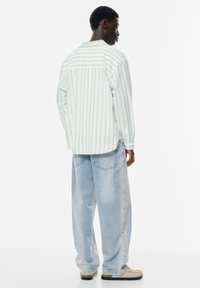 Langärmliges, hellblau gestreiftes Hemd aus Baumwolle, kombiniert mit locker sitzenden, hellen Jeans. Verfügt über Knopfmanschetten und ein Rückenteil mit einer yoke-Design.