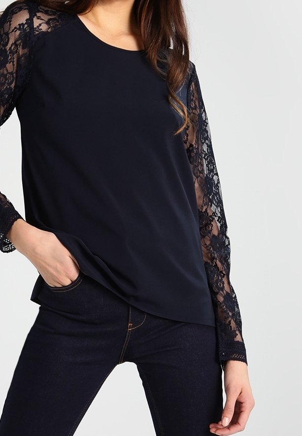 Haut bleu marine avec manches longues en dentelle, encolure ronde et coupe décontractée. Tissu lisse, texture contrastée de la dentelle ajoutant du détail.