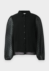 Blouse noire avec un buste uni à pois texturés et des manches bouffantes transparentes. Fermeture à boutons à l'avant, col rond et manches ourlées.