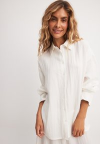 Witte button-up blouse van lichtgewicht stof met een gekreukte textuur, met een puntkraag en lange mouwen met opgerolde manchetten.
