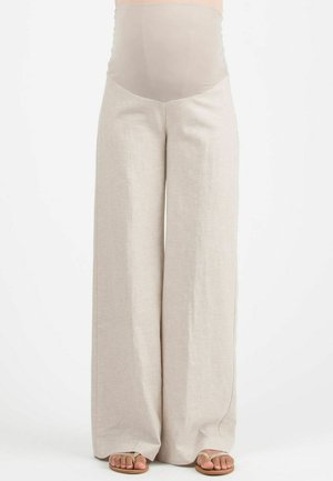 Beige wijde zwangerschapsbroek met doorzichtig hoog taillepaneel, gedragen met bruine teenslippers, getoond van midden torso tot voeten op een witte achtergrond.