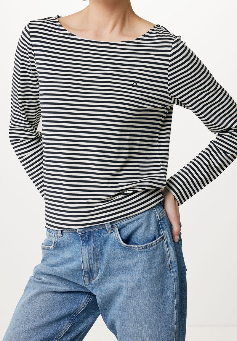 Svart och vit randig långärmad topp med båtringning och tajta ärmslut. Matchad med ljusblå, avslappnade jeans.