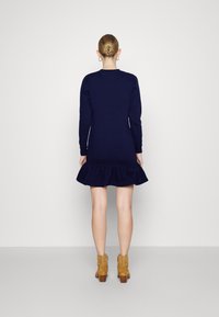 Marinblå stickad klänning med långärmar och en utsvängd volangnederdel, i kombination med bruna ankelboots. Slät textur och åtsittande silhuett.